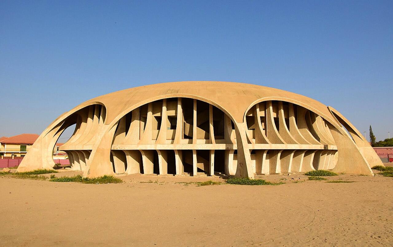 Edifício em betão de forma arredondada sob céu azul, no Namibe