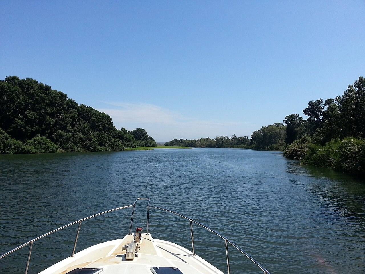 Proa de um barco a navegar no rio Kwanza entre margens verdes
