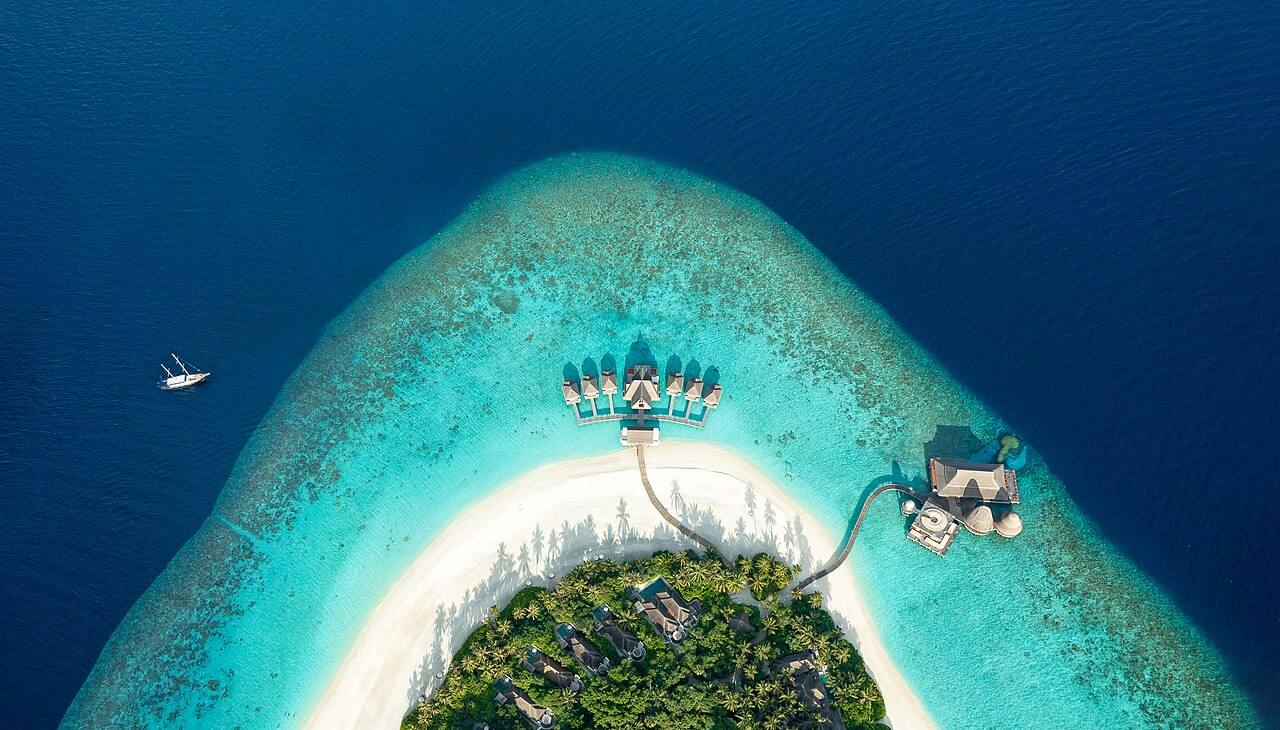 Vista aérea de uma ilha com praia e villas sobre a água, nas Maldivas