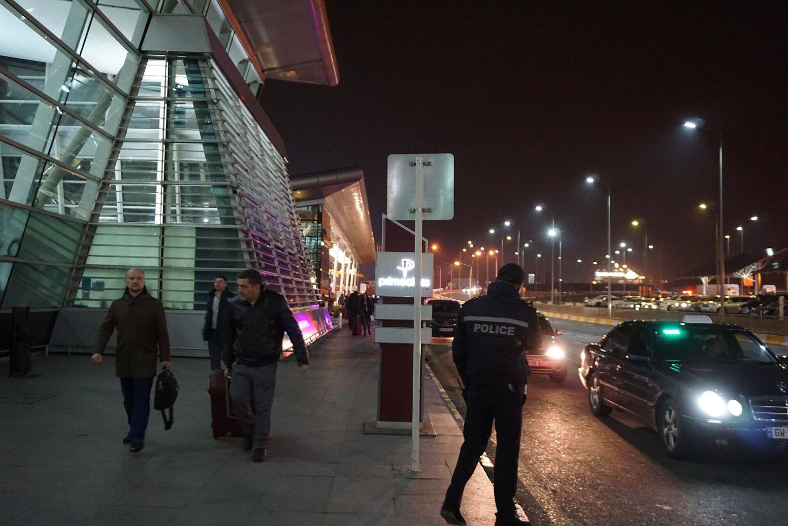 Chegadas de um aeroporto à noite, com viaturas e passageiros
